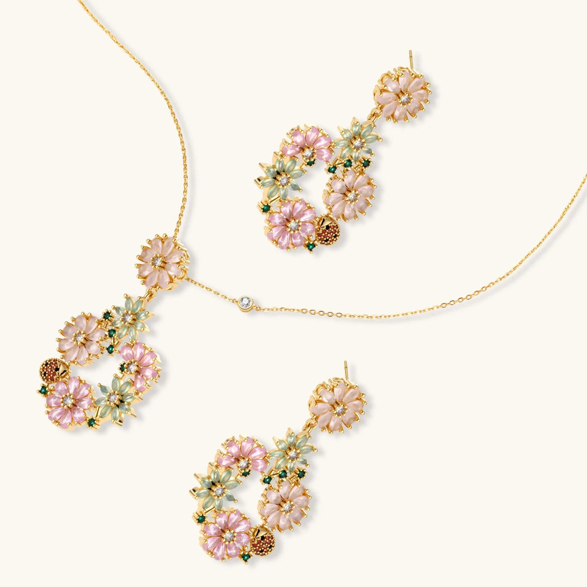 14K gold plated jewelry set with pink and green cubic zirconia flowers arranged in wreath design on cream background