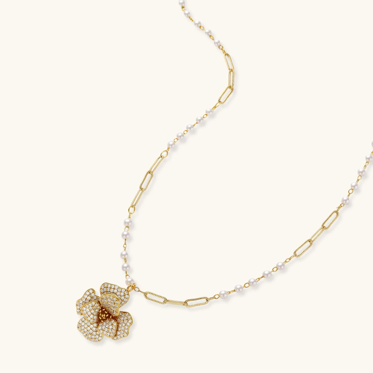 Gold plated flower pendant necklace with white beads and matching cubic zirconia flower stud earrings on a cream background.