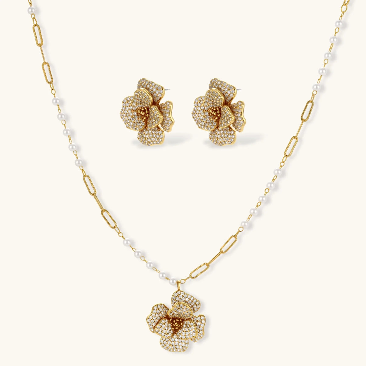 Gold plated flower pendant necklace with white beads and matching cubic zirconia flower stud earrings on a cream background.