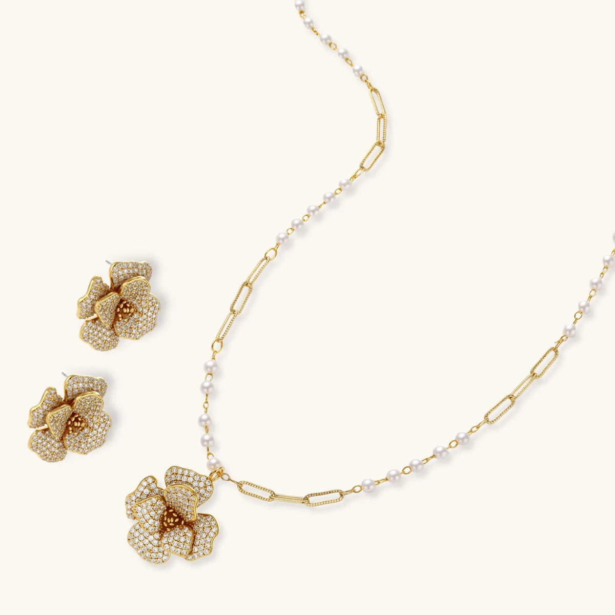 Gold plated flower pendant necklace with white beads and matching cubic zirconia flower stud earrings on a cream background.