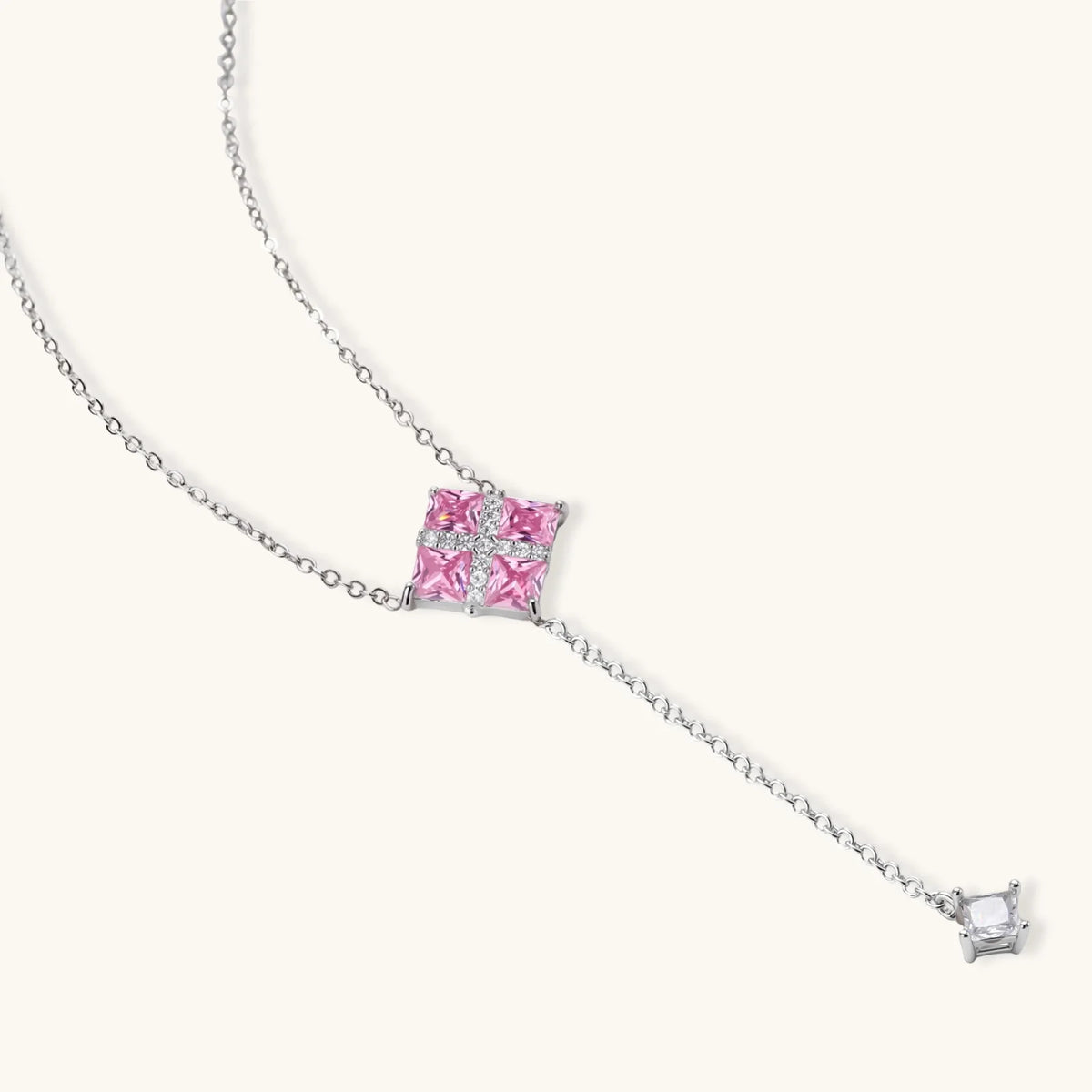 Necklace and stud earrings set with four pink square zirconia stones and a white crossed band, on a cream background.