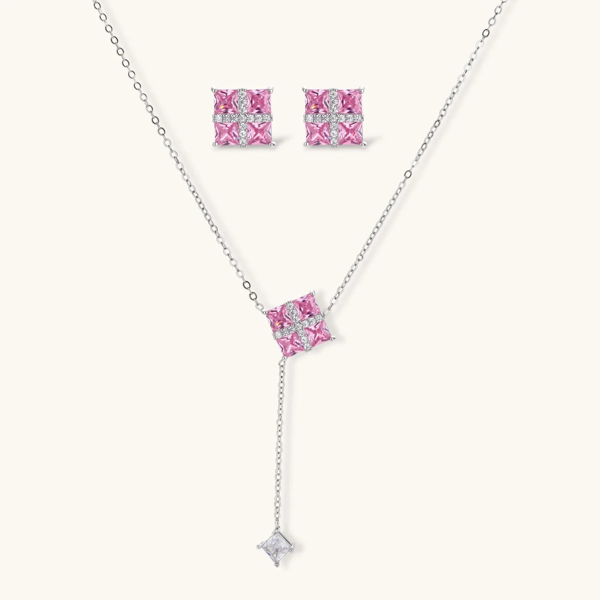 Necklace and stud earrings set with four pink square zirconia stones and a white crossed band, on a cream background.