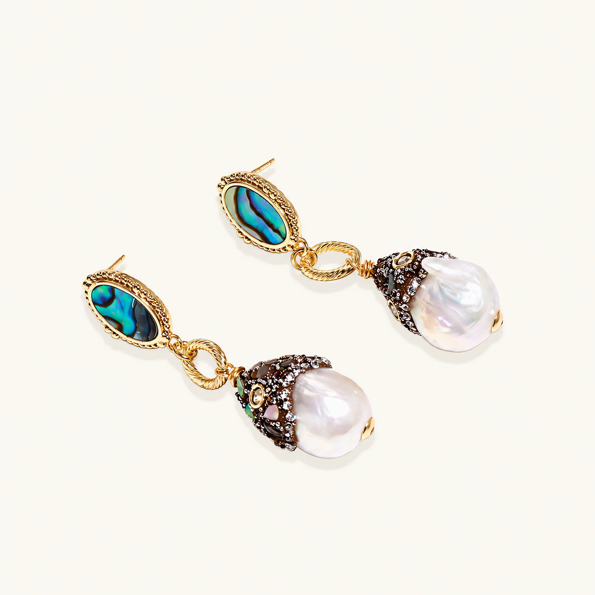 Gold drop earrings with iridescent abalone studs, rope links, jeweled caps and white baroque pearls on cream background