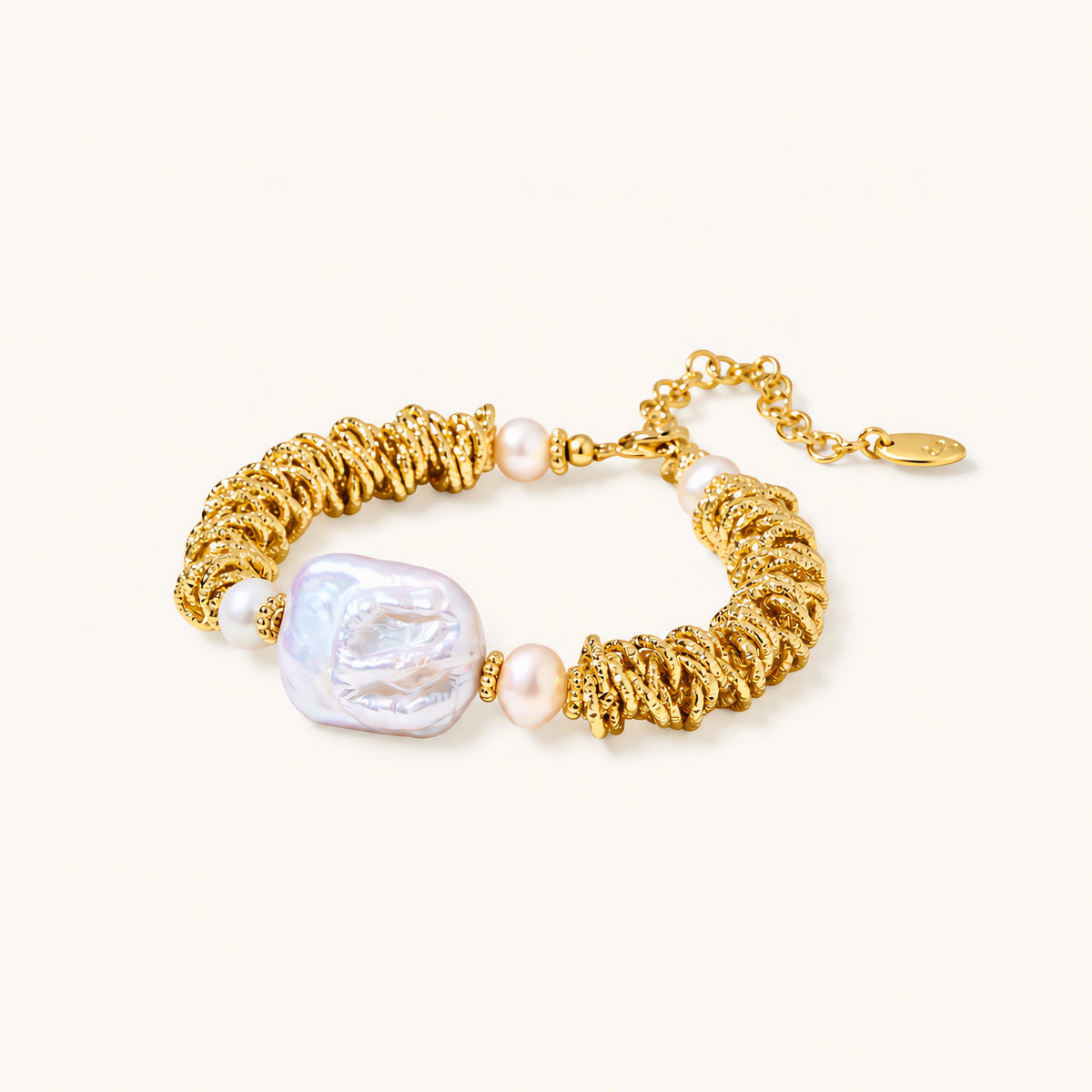 18k gold-plated bracelet with textured wave segments, baroque pearl centerpiece, and round freshwater pearls on cream background