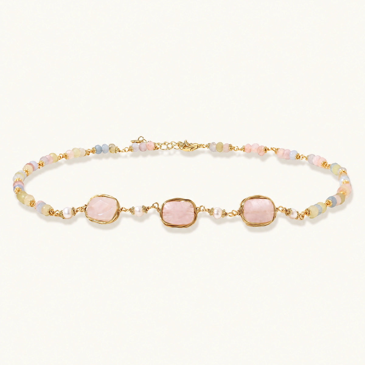 Gold necklace with three rose quartz stones, multicolor pastel beads, and pearl accents on white background.