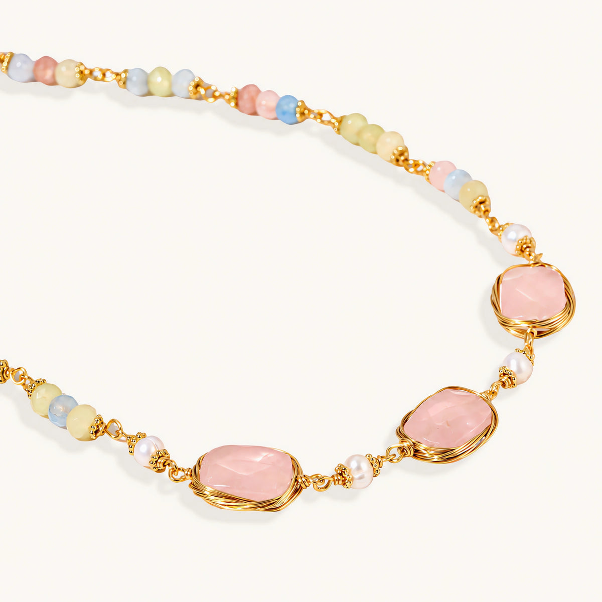 Gold necklace with three rose quartz stones, multicolor pastel beads, and pearl accents on white background.