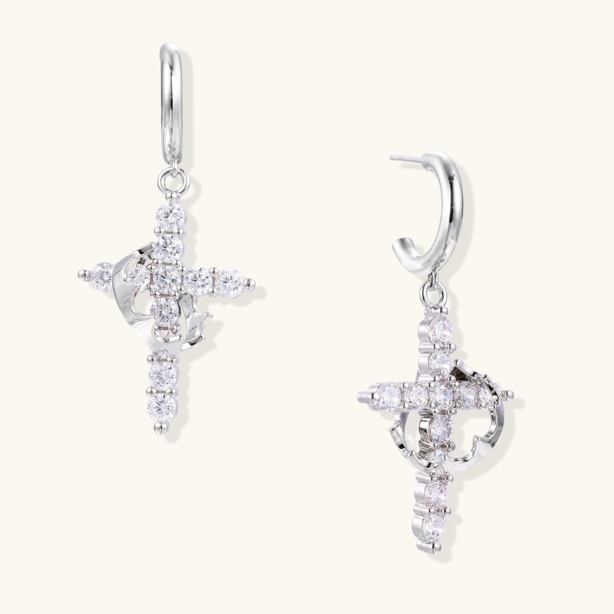 White gold-plated hoop earrings with sparkling zirconia cross charms dangling against cream background