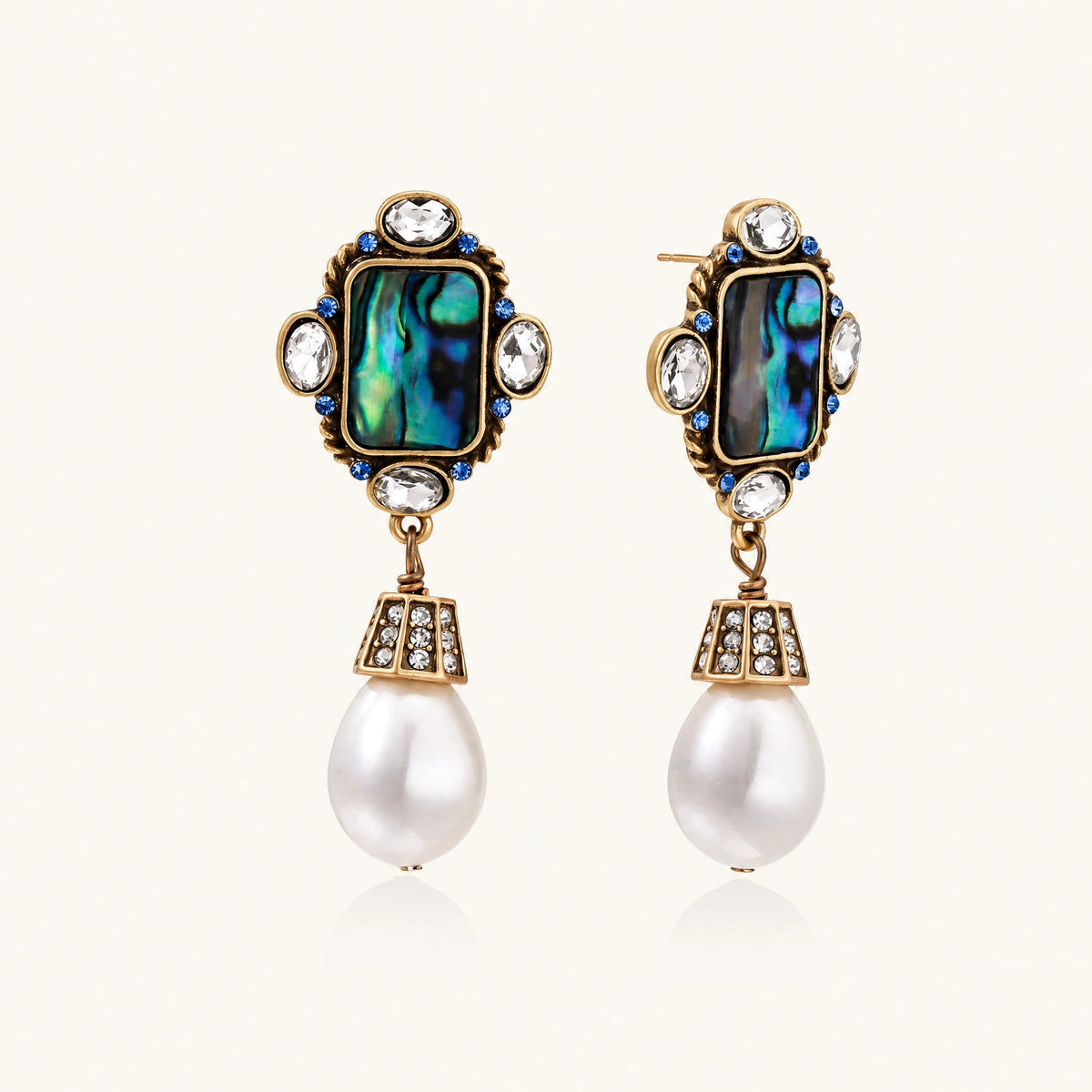 Pair of vintage-style gold plated drop earrings with iridescent abalone shell panels, clear and blue crystals, and white teardrop beads.
