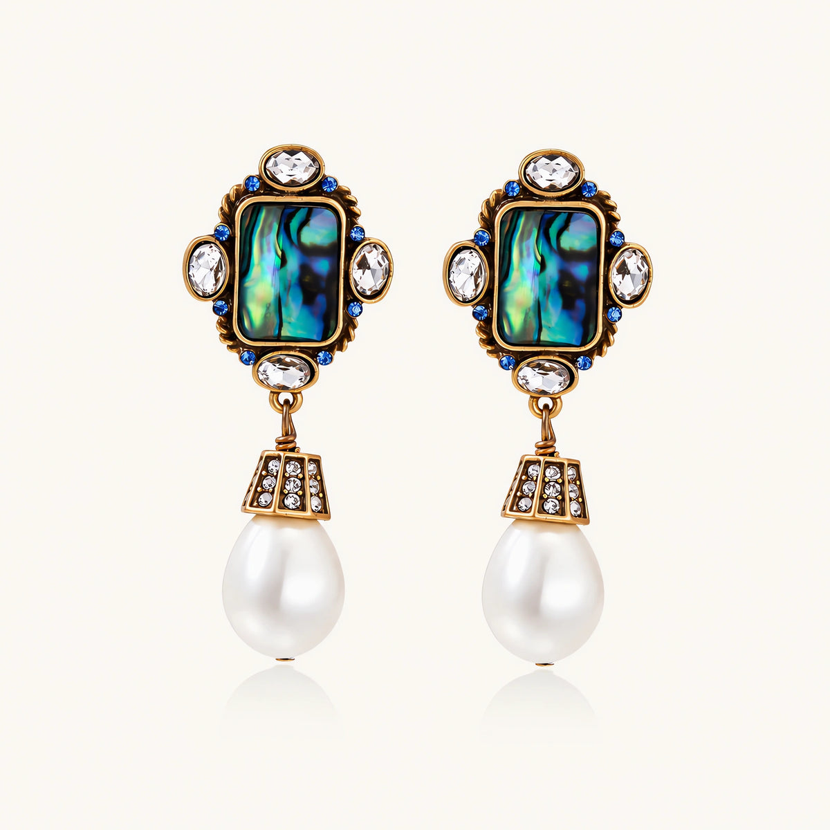 Pair of vintage-style gold plated drop earrings with iridescent abalone shell panels, clear and blue crystals, and white teardrop beads.