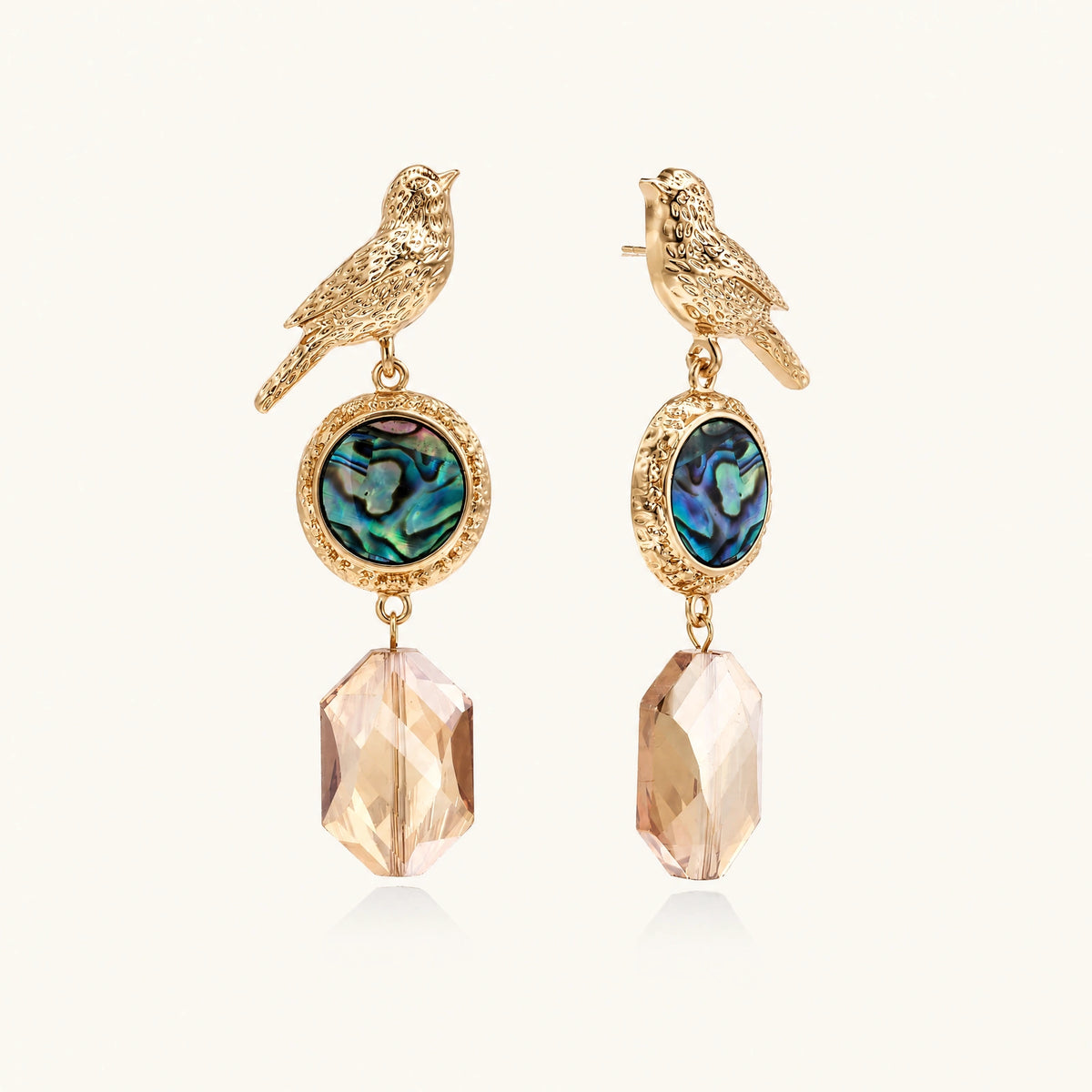 Gold-plated bird stud earrings with iridescent abalone shell medallions and champagne crystal drops on cream background