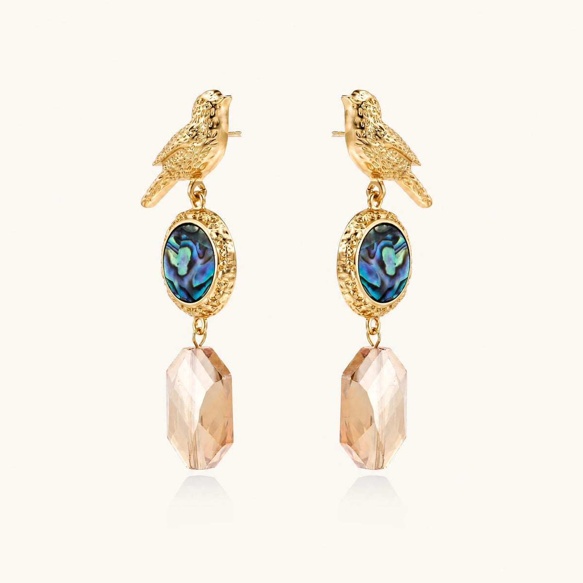 Gold-plated bird stud earrings with iridescent abalone shell medallions and champagne crystal drops on cream background