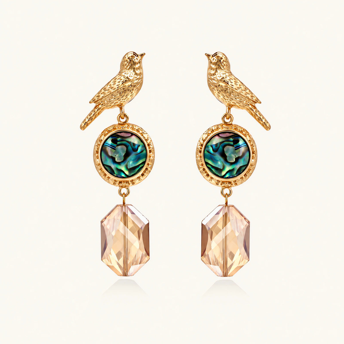 Gold-plated bird stud earrings with iridescent abalone shell medallions and champagne crystal drops on cream background