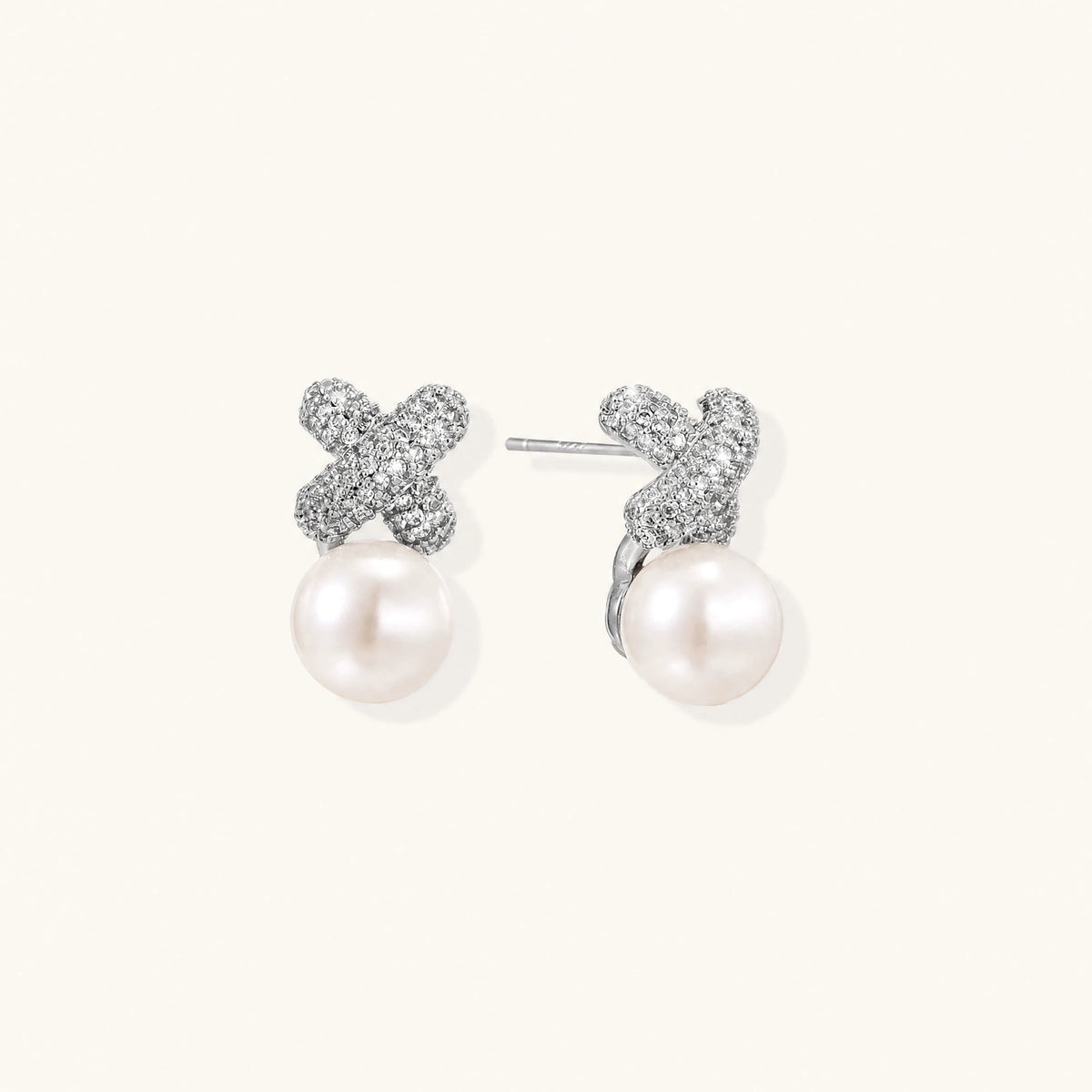 White gold plated studs featuring pavé X-shaped tops with freshwater pearl drops on cream background.