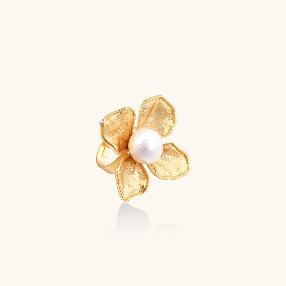 Gold-plated flower ring with textured petals and white cotton pearl center on cream background