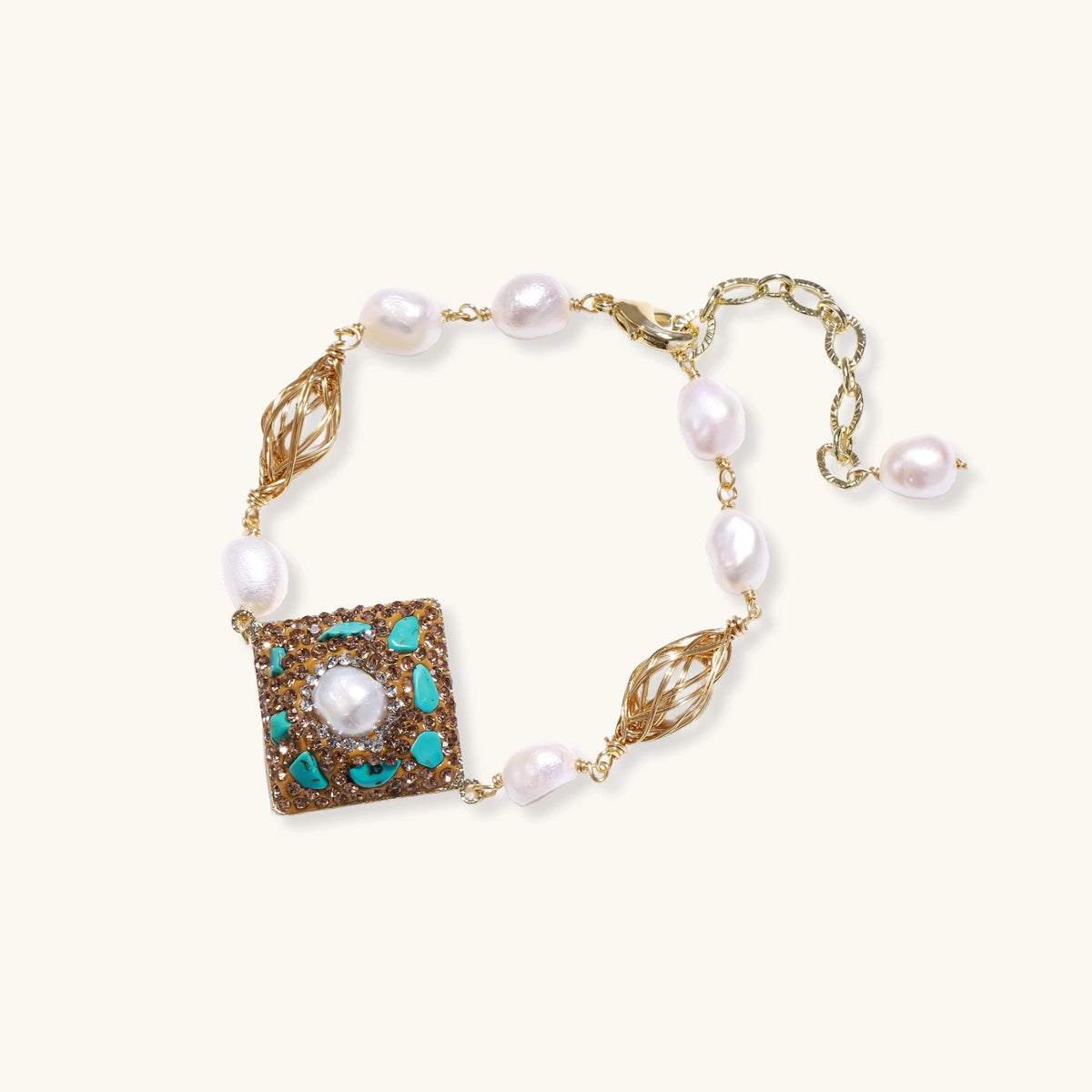 Gold-plated bracelet with baroque centerpiece, turquoise stones, freshwater pearls, and ornate chain links on cream background.