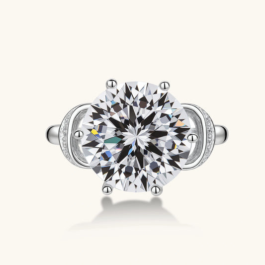 Sterling silver ring with 5ct round moissanite center stone and intricate bow design with pavé accents on white background.