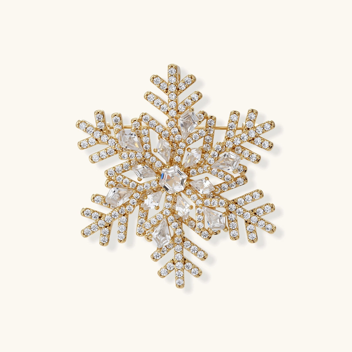Ornate gold-plated snowflake brooch with geometric crystal pattern and sparkling zirconia stones on cream background.